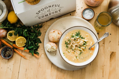 Open Spoonful of Comfort Chicken Noodle Soup Package on table with bowl of soup and rolls.